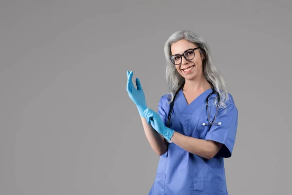 Radosna Lekarka Zakładająca Rękawiczki Medyczne Przed Wizytą Pozująca Okularach Niebieskim — Zdjęcie stockowe