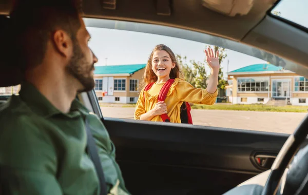 做父母和早起的例行公事 快乐的小学女生上学 和坐在车里的爸爸挥手道别 全神贯注地看着女生 — 图库照片