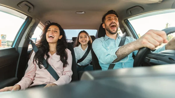Excited european family of three riding car and singing, enjoy traveling by automobile, parents and daughter enjoying auto ride together on weekend