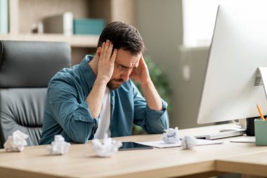 İlham Krizi. Masasında buruşuk kağıtlarla işyerinde oturan düşünceli genç işadamı, umutsuzluk içinde kafaya dokunan erkek girişimci, ofiste acı çeken sorunlar, boş alan