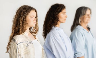 Sakin, ciddi, beyaz bir genç kız, bin yıllık anne ve yaşlı büyükanne, beyaz stüdyo arka planında soyutlanmış. Kadın nesli, genetik, aşk, ilişki ve aile, güzellik, yaşam tarzı