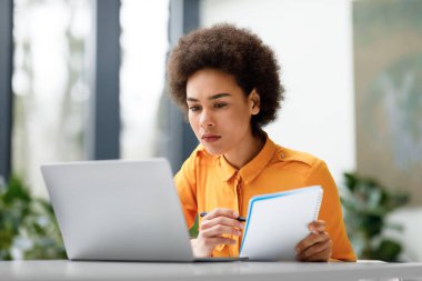 Uzaktan eğitim. Odaklanmış Latin bayan dizüstü bilgisayarla video dersi izliyor ve not alıyor, sanal ders öğreniyor, yararlı bilgiler yazıyor.