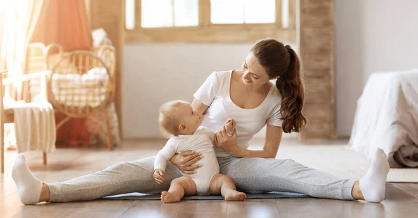 Mom and child fitness. Happy athletic young mother training stretching with her little baby toddler at home. Mom doing regular workout on yoga mat with cute blonde infant son, panorama