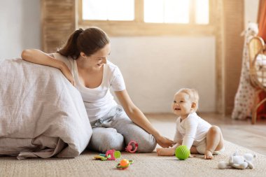Genç ve mutlu bir anne evde meraklı küçük bir bebekle yerde oynuyor. Gülümseyen anne, küçük bir bebekle komik bir aktivite içinde. Çocuk bakımı kavramı, kopyalama alanı