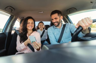Araba navigasyon uygulaması. Mutlu bir kadın cep telefonuyla şoföre GPS uygulaması gösteriyor. Aile seyahati, araç kullanma, hafta sonu gezisi.