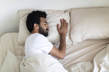 Sakin, genç Hintli bir adam rahat bir yatakta uyuyor. Yakışıklı, bin yıllık doğu çocuğu yatak odasındaki yorganın altında uyukluyor. Sağlıklı uykuların tadını çıkarıyor.