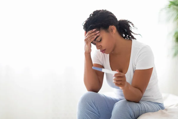 可悲的年轻黑人妇女坐在床上检查自己最近的怀孕测试 令面临意外生育或无法怀孕 健康问题的非洲裔美国妇女心烦意乱 — 图库照片