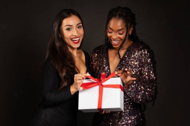 Noel hediyesi. Çok ırklı, güzel, siyah stüdyo arka planında duran hediye kutusunu tutan kız arkadaşların kutlu olsun. Kış bayramı kutlaması, Yeni Yıl Kutlaması ve Noel Hediyeleri konsepti