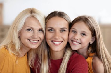 Aile ilişkisi ve yakınlık. Pozitif neşeli beyaz aile reşit olmayan bir kızın yakın plan portresi, milenyum kadını ve büyükanne kıdemli bayan evde birlikte poz veriyor, kameraya gülümsüyor.
