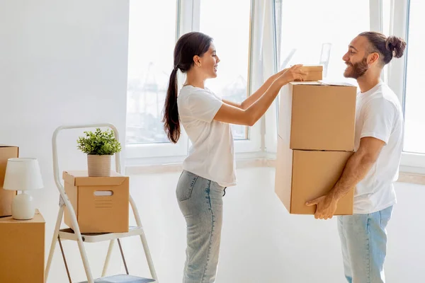 Happy young spouses packing boxes for moving, relocating to new apartment standing at home. Real esate rent, mortgage and ownership concept. Family millennial couple preparing to move house