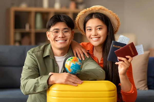 笑着的日本游客夫妇手持旅游票和护照 在家中与手提箱和世界各国合影 对着相机微笑的肖像 年轻的环球旅行者去度蜜月 — 图库照片