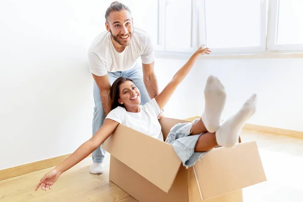 Playful young multiracial couple having fun in their home on relocation day. Millennial woman and her boyfriend playing together with carton box while moving to new apartment, changing house