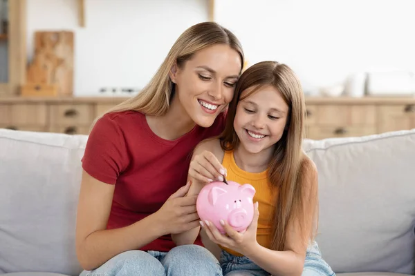 Setting good example. Young parent mother teach child little daughter girl to manage finances save money spend earnings with economy plan family budget. Friendly mom and kid thrift coins in piggybank