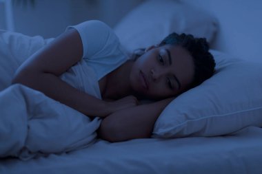 Uyanık, uykusuz, üzgün, siyah bir kadın gece yatakta tek başına yatıyor, uyuyamıyor, kendini yalnız hissediyor, depresyon ya da kaygı yaşıyor, uyumakta güçlük çekiyor, evde dinleniyor.
