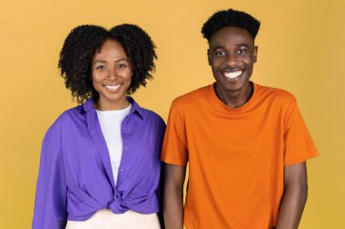 Bin yıllık yakışıklı siyahi kadın ve kameraya gelişigüzel bakan adam sarı stüdyo arka planında izole edilmiş, yakın plan. Yaşam tarzı, öğrenim, boş zamanlardaki randevu, reklam ve teklif