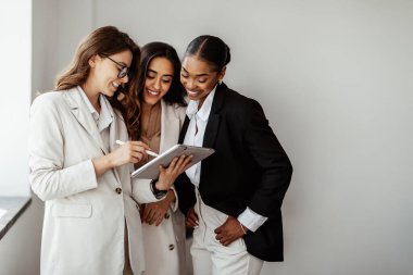 Modern dijital tablet kullanan mutlu çok ırklı iş kadınları ofiste yeni fikirler ve projeler tartışıyorlar, boş alan. Takım çalışması ve işbirliği kavramı