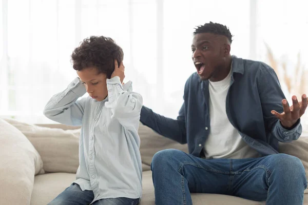 児童虐待問題 怒っている黒人の父親が怖がった小さな息子を抱きしめながら 不幸なキッドボーイが家で耳を覆っている 家庭問題と家庭内暴力 攻撃的な父親の概念 選択的フォーカス — ストック写真