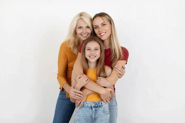 Love, family, affection concept. Beautiful preteen girl, millennial woman and senior lady bonding posing on white background. Happy three generations mother, daughter and grandmother embracing