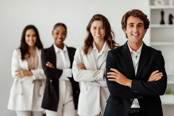 Male leadership concept. Diverse business team standing in line with folded arms and smiling at camera posing in office, selective focus on businessman