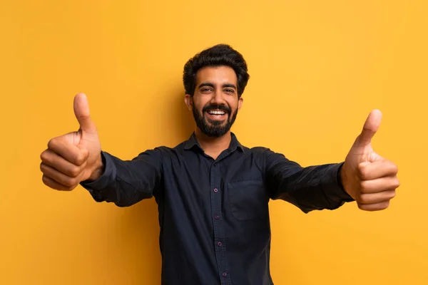 カメラで親指を示す陽気で幸せなインド人男性 ポジティブな若い東部男性 何かをお勧め スタジオで黄色の背景の上に立っている間承認の兆候をジェスチャー コピースペース — ストック写真