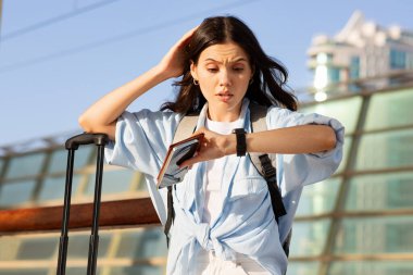 Üzgün, kafası karışık, sırt çantalı, bileti ve telefonu olan genç Avrupalı kadın saate bakıyor, uçağa geç kalıyor, istasyonda ve dışarıda ulaşımı kaybediyor. Seyahat zamanı, seyahat sorunları, hata