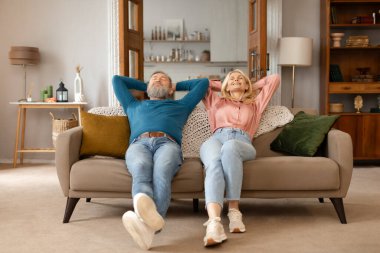 Huzurlu Son Sınıf Eşleri, gözleri kapalı, kanepeye yaslanmış, evdeki rahat koltuğun keyfini çıkarıyorlar. Çiftin Tam Uzunluğu Elleri Başının Arkasında Otururken Rahatlıyor