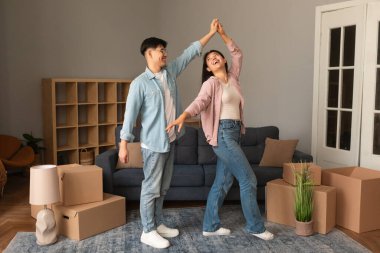 Harika bir emlak teklifi. Taşınan Kutular Arasında Genç Asyalı Çiftler Dansı, Yeni Ev Alışverişini kutlamak, Ev İçlerinde İki Kişilik Ev Partisi. Daire Kiralama ve Sahiplik