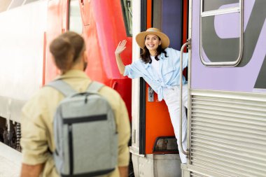 Genç Avrupalı adam mutlu bir kadınla karşılaşıyor, istasyonda, dışarıda trende el sallıyor. Seyahat, turistik duygular, aktif yaşam tarzı, yaz tatili, veda işareti, aşk ve ilişki