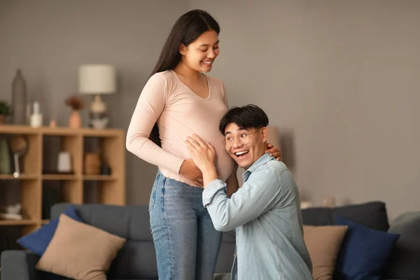 Feliz Marido Asiático Escuchando Esposa Embarazada Vientre Interior Del Hogar —  Fotos de Stock