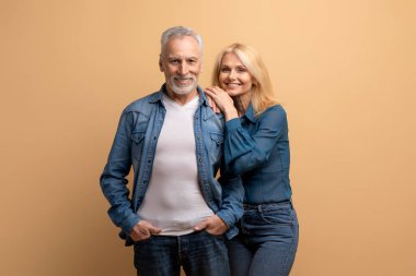 Aşk, evlilik, sevgi, ilişki kavramı. Mutlu bir evliliği olan Kafkasyalı yaşlı erkek ve kadın kot elbiseli bej arka planda kameraya sarılıp gülümsüyor.