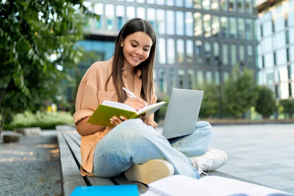 陽気でかわいいヒスパニック系の若い女性学生が大学のキャンパスでベンチに座り 授業の準備をし ノートパソコンを使ってメモを取ります 教育オンラインコースに参加するスマートな女性 — ストック写真