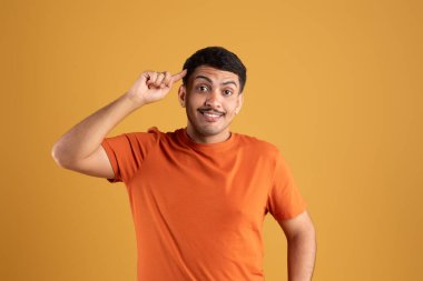 Heyecanlı Brezilyalı adam gülümsüyor, tek parmağıyla kafasını işaret ediyor, harika bir fikir ya da düşünce, iyi bir hafıza, sarı stüdyo arka planında duruyor.