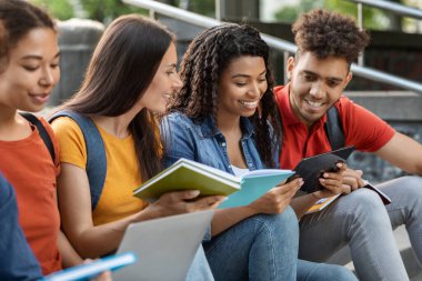 Çeşitli etnik çeşitlilikte öğrenci kitap okuyor ve dışarıda dijital tablet kullanıyor. Sınavlara birlikte hazırlanan bir grup genç erkek ve kadın çalışmanın keyfini çıkarıyor. Derslerden önce hazırlanıyor.