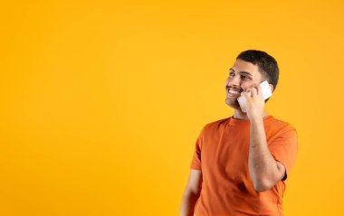 Cep telefonuyla konuşan mutlu Brezilyalı adam, boş alana bakıyor, pozitif telefon konuşmaları yapıyor, sarı arka planda stüdyoda duruyor. Mobil iletişim konsepti