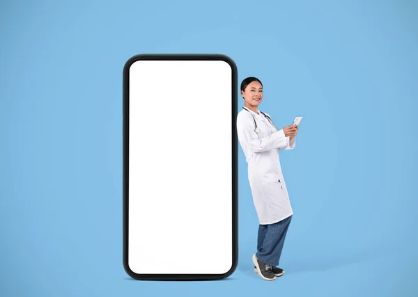Uśmiechnięta Piękna Azjatycka Lekarka Stojąca Obok Dużego Pustego Smartfona Białym — Zdjęcie stockowe