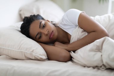 Depresyondaki Afro-Amerikan kadın portresi, yatakta yatan, genç siyahi bayanın evde dinlenirken uykusuzluk çekmesi, duyarsızlık ve depresyon sorunu, yakın çekim,