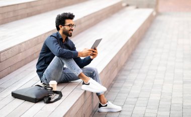 Keyifli, şık Hintli genç adam işten sonra dışarıda takılıyor, şehir merkezindeki merdivenlerde oturuyor, paket kahve içiyor, dijital tablet kullanıyor, arkadaşlarıyla sohbet ediyor, mekanı kopyalıyor.