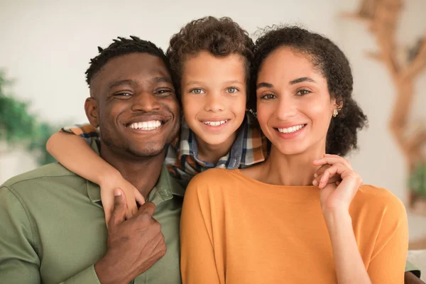 Loving Family. Cheerful Diverse Parents And Kid Son Hugging Smiling To Camera At Home Interior, Portrait Shot Of Happy Black Father, Middle Eastern Mother And Their Child Boy
