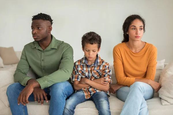 家族の不幸と紛争 多様な親の間で座っている不幸な子供の少年 彼らはクォーレル後に沈む間 離婚と分離を考えて ホームでの関係で問題を抱えています — ストック写真