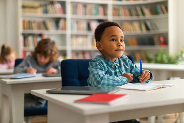 教育知識コンセプト 小学校の教室で机に座り 先生の話を聞き 見ているスマートな黒人の少年 教室でノートを書く子供たち — ストック写真