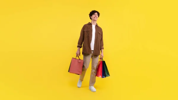 セールス 消費者主義 ショッピング後の笑顔の男は 黄色の背景にポーズする多くの色のパッケージバッグ スタジオショット 顧客は購入広告の提供と立っています パノラマ — ストック写真