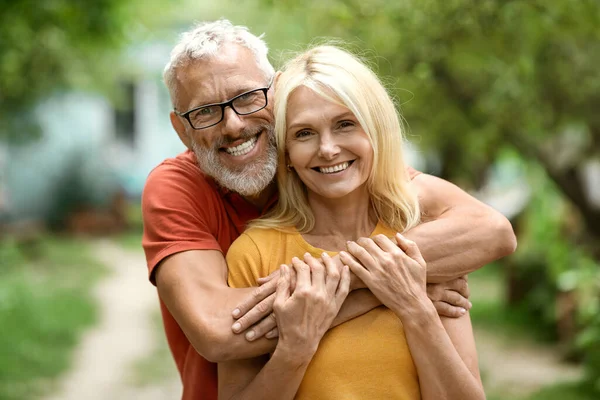 Portrait Of Beautiful Happy Senior Couple Posing Outdoors In Garden, Romantic Mature Spouses Embracing And Smiling At Camera, Relaxing Together On Backyard, Enjoying Retirement Leisure, Copy Space