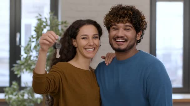 房屋所有权 一对快乐的中东年轻夫妇的画像 展示钥匙 站在自己的新公寓里 拥抱在一起 微笑着拍照 — 图库视频影像