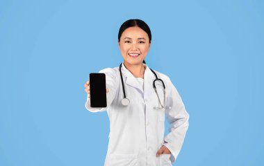 Tıbbi Hizmetler. Elinde boş ekranla gülümseyen Asyalı doktor bayan elinde akıllı telefon, üniformalı terapist kadın boş cep telefonunu gösteriyor, cep telefonu uygulaması ya da web sitesi öneriyor,