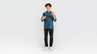 Telefon ve kredi kartı ile online alışveriş yapan beyaz stüdyo geçmişi olan genç bir adam. Boş alanı olan panoramik pankart, mobil bankacılık uygulaması kullanan akıllı telefonu olan müşteri