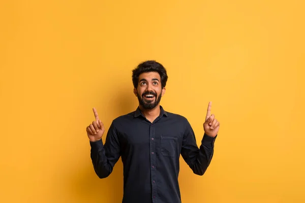 Adのための場所 エキサイティングな若いインドの男性は 2つの手で黄色の背景のコピースペースを指摘し 幸せな東部男性は 広告やデザインのための彼の上の領域を示しています — ストック写真