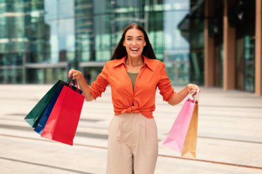 Alışveriş neşesi. Heyecanlı duygusal Kafkasyalı kadın şehir merkezinde bir sürü alışveriş çantası tutuyor, dışarıda duruyor ve alışveriş paketlerini heyecanla gösteriyor, kameraya gülümsüyor.