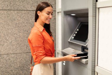 Finansal işlemler, para çekme. Gülümseyen kadın telefonu ATM okuyucusuna veriyor, dışarıdaki banka hesabından para çekiyor. Müşteri ATM 'ye ulaşmak için akıllı telefon kullanıyor