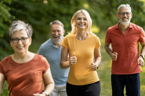 Group of sporty mature people jogging at park together, happy senior men and women running outdoors, active older adults in sportswear exercising outside, enjoying healthy lifestyle, closeup