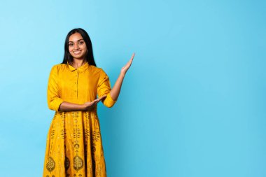 Moda Teklifi. Geleneksel sarı işlemeli sıradan elbiseler giyen, mavi arkaplanda duran boş yerleri gösteren güzel Hintli genç bir kadın. Stüdyo Çekimi